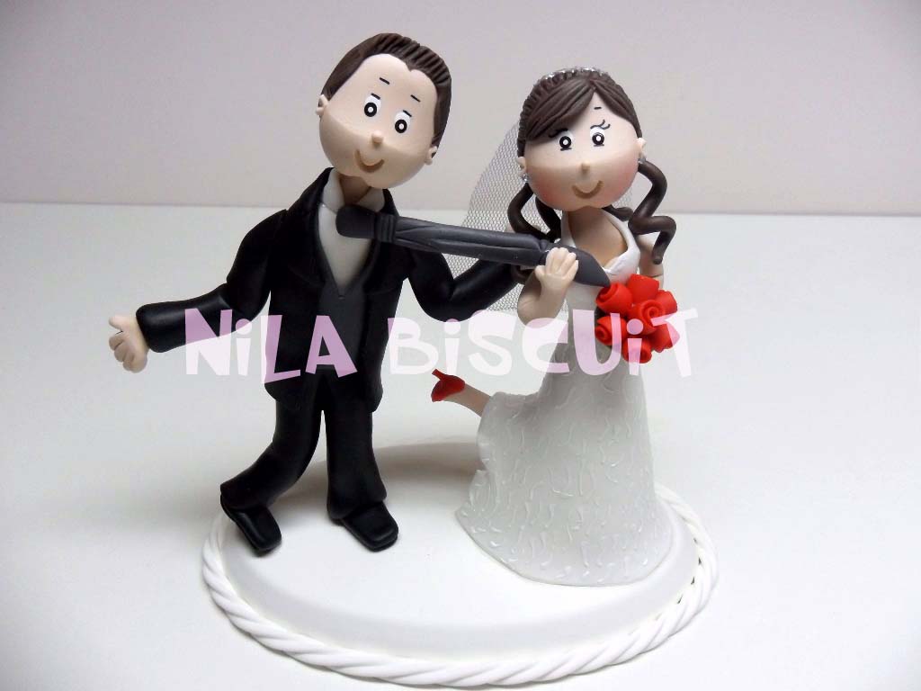 Bonecos do bolo de casamento com a noiva puxando o noivo pela gravata e com o pé levantado
