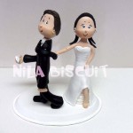 Bonecos do bolo de casamento com a noiva puxando pela gravata e mostando o pé