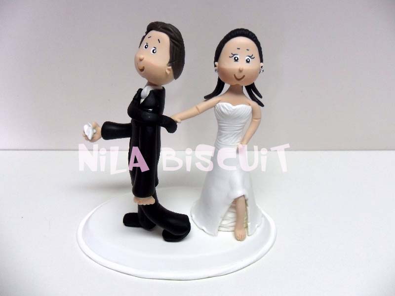 Bonecos do bolo de casamento com a noiva puxando pela gravata e mostando o pé