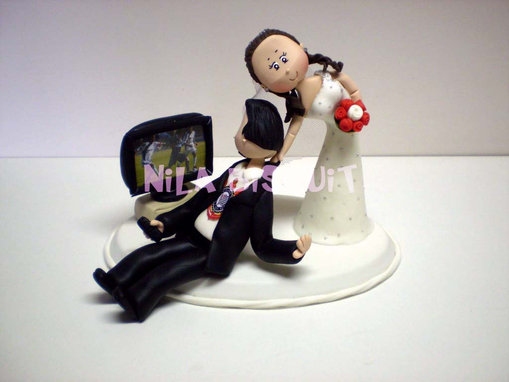 Bonequinhos do bolo de casamento com noivo corinthiano assistindo jogo de futebol e noiva puxando ele