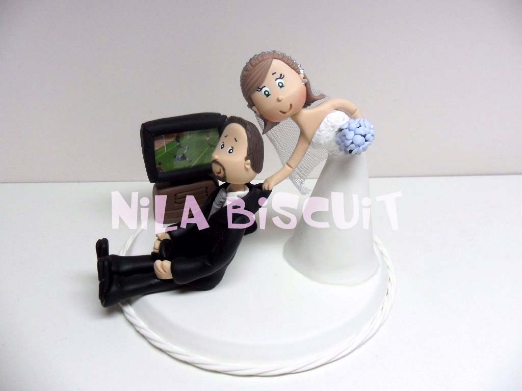 Bonequinhos do bolo de casamento com noivo jogando video game de futebol e noiva puxando ele